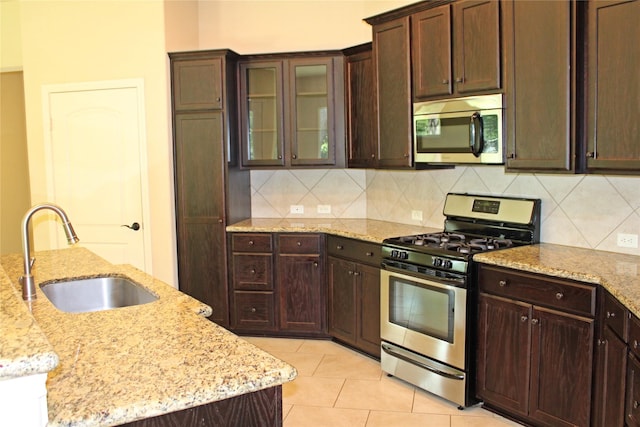 kitchen with stainless steel appliances, sink, light stone counters, tasteful backsplash, and a center island with sink