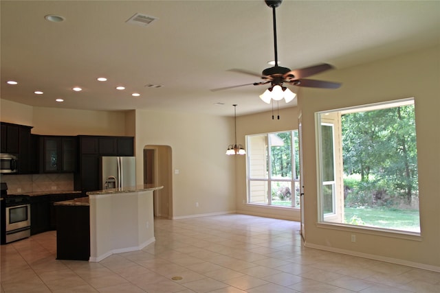 kitchen with a center island with sink, stainless steel appliances, light stone countertops, visible vents, and glass insert cabinets