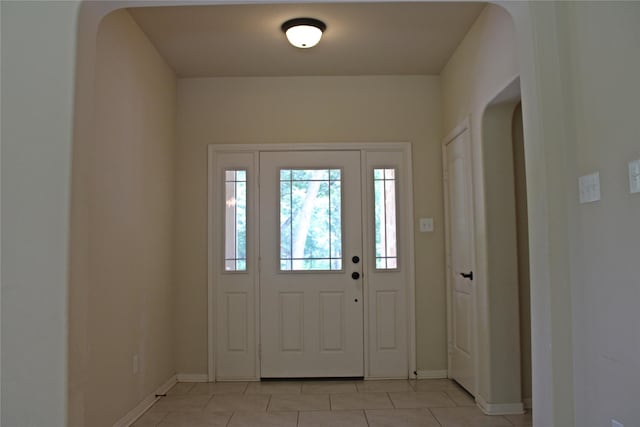 foyer entrance with baseboards, light tile patterned floors, and arched walkways