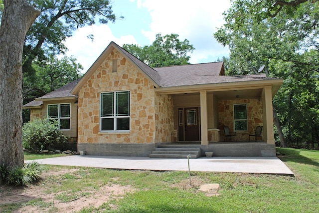 rear view of property with roof with shingles, a yard, and stone siding