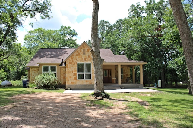 view of front of house with roof with shingles, a patio, stone siding, and a front yard