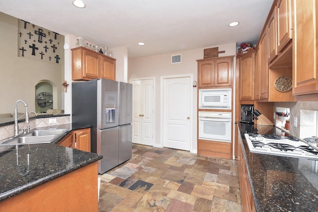 kitchen featuring white appliances, dark stone countertops, tasteful backsplash, and sink