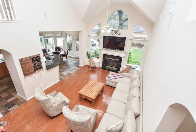 living room with high vaulted ceiling, a tiled fireplace, ceiling fan, and hardwood / wood-style floors