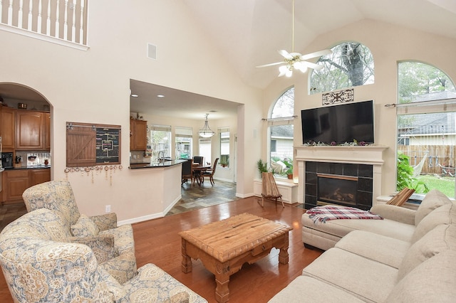 living room featuring high vaulted ceiling, a tiled fireplace, wood-type flooring, and ceiling fan