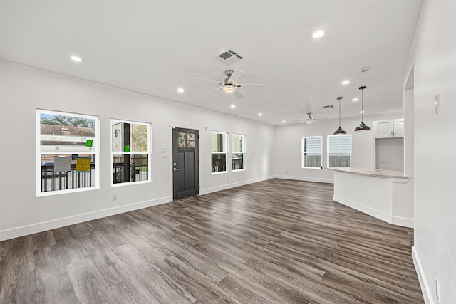 unfurnished living room featuring ceiling fan, dark wood-type flooring, and a wealth of natural light