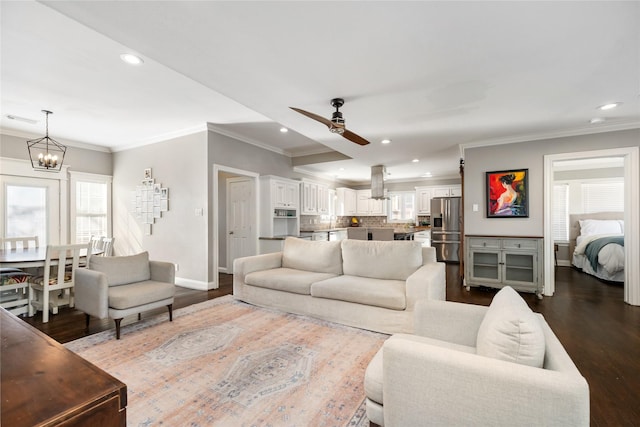 living room with dark wood-type flooring, crown molding, and ceiling fan with notable chandelier