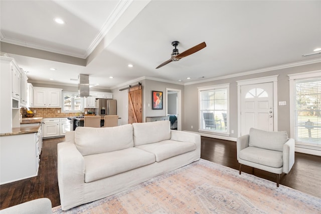 living room featuring dark wood-type flooring, ceiling fan, a barn door, and crown molding