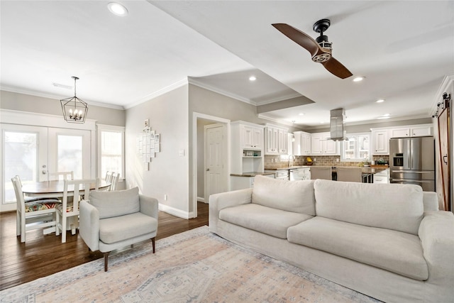 living room featuring a barn door, ornamental molding, french doors, hardwood / wood-style flooring, and ceiling fan with notable chandelier