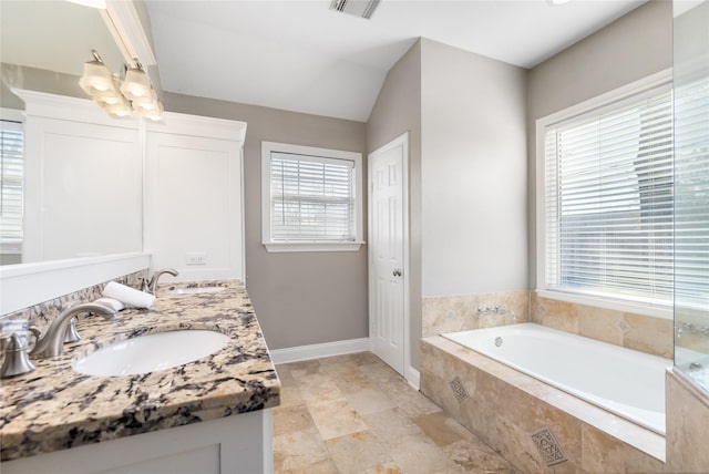 bathroom with vaulted ceiling, a relaxing tiled tub, a healthy amount of sunlight, and vanity