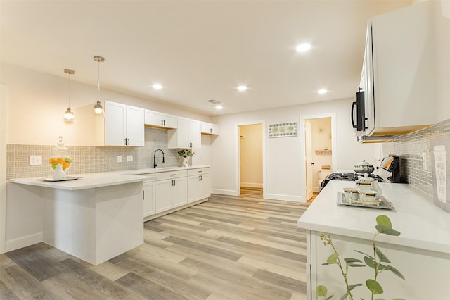 kitchen with decorative light fixtures, white cabinets, stove, kitchen peninsula, and backsplash