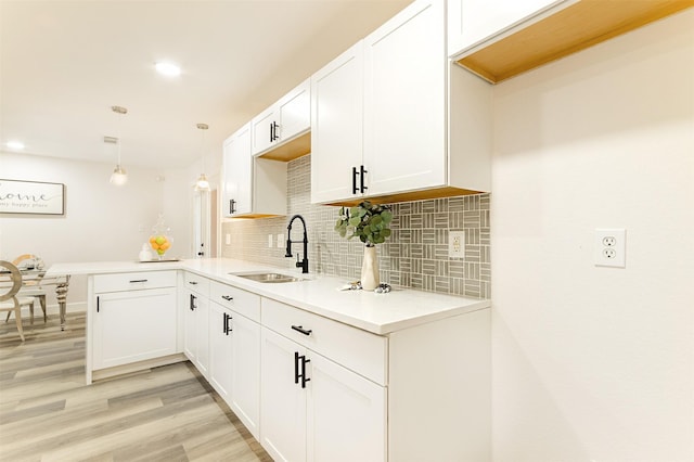 kitchen with kitchen peninsula, pendant lighting, tasteful backsplash, white cabinetry, and sink