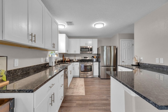 kitchen with stainless steel appliances, a textured ceiling, dark stone countertops, and white cabinets