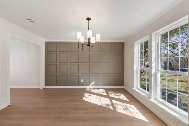 unfurnished dining area featuring light hardwood / wood-style floors, crown molding, and an inviting chandelier