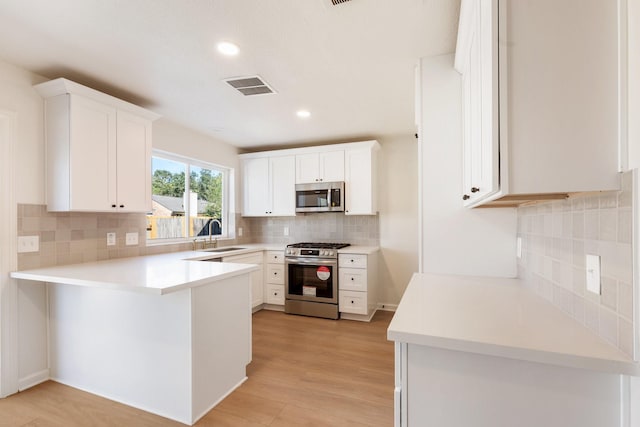 kitchen with white cabinetry, kitchen peninsula, appliances with stainless steel finishes, light wood-type flooring, and sink