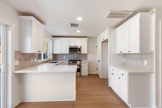 kitchen with kitchen peninsula, appliances with stainless steel finishes, white cabinetry, and sink