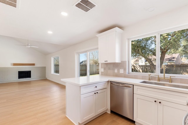 kitchen with white cabinetry, sink, kitchen peninsula, a brick fireplace, and stainless steel dishwasher