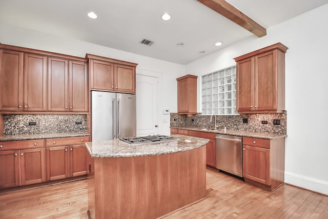 kitchen with light stone countertops, a center island, light wood-type flooring, beam ceiling, and appliances with stainless steel finishes