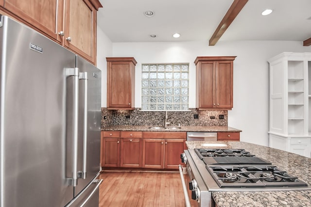 kitchen with appliances with stainless steel finishes, light stone counters, beam ceiling, sink, and light hardwood / wood-style flooring