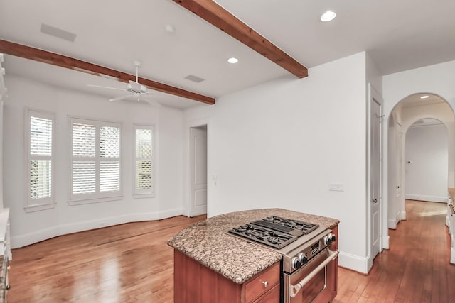 kitchen featuring light wood-type flooring, beamed ceiling, ceiling fan, light stone counters, and stainless steel range with gas cooktop