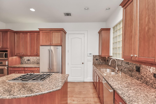 kitchen with sink, light stone counters, light wood-type flooring, a kitchen island, and appliances with stainless steel finishes