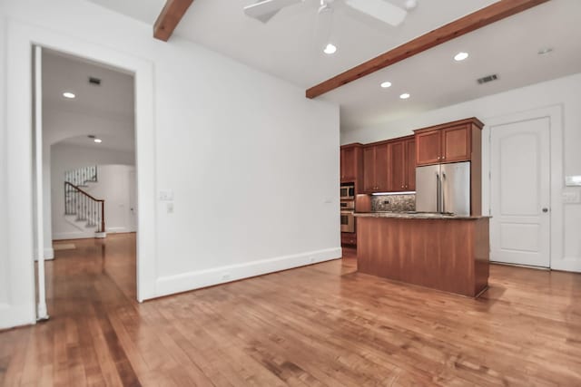 kitchen with appliances with stainless steel finishes, a kitchen island, backsplash, and beamed ceiling