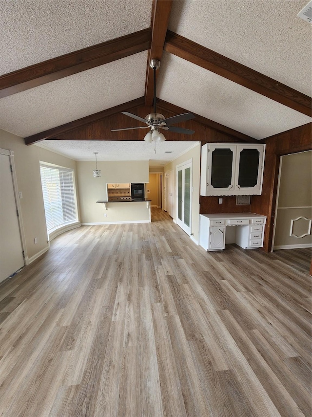 unfurnished living room with a textured ceiling, built in desk, light wood-type flooring, ceiling fan, and vaulted ceiling with beams