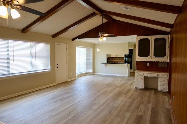 unfurnished living room featuring ceiling fan, light hardwood / wood-style floors, lofted ceiling with beams, and a wealth of natural light