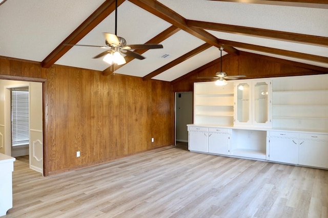 unfurnished living room featuring ceiling fan, light hardwood / wood-style floors, lofted ceiling with beams, and wood walls