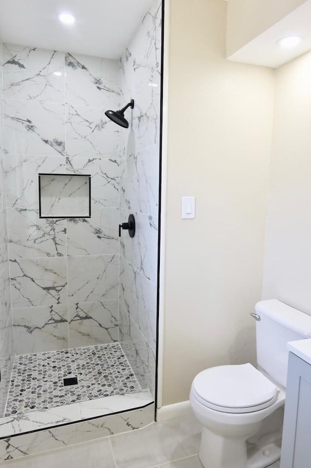 bathroom with toilet, a tile shower, vanity, and tile patterned flooring