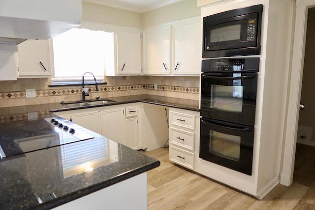 kitchen featuring black appliances, light wood-type flooring, white cabinets, dark stone countertops, and sink