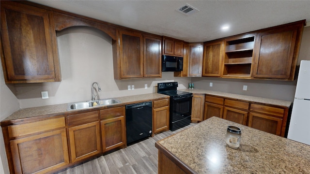 kitchen with light hardwood / wood-style flooring, light stone countertops, black appliances, and sink