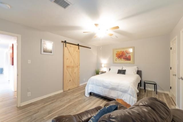 bedroom with a barn door, visible vents, light wood-style flooring, and baseboards