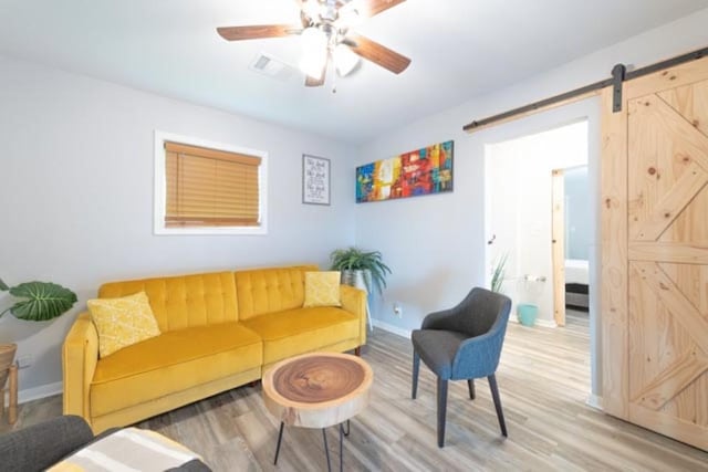 living room with a ceiling fan, light wood-type flooring, baseboards, and a barn door