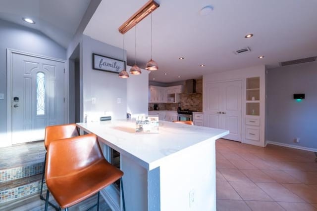 kitchen with a breakfast bar area, hanging light fixtures, light countertops, stainless steel stove, and wall chimney range hood