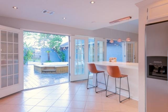 kitchen featuring stainless steel fridge, white cabinets, a breakfast bar, light countertops, and light tile patterned flooring