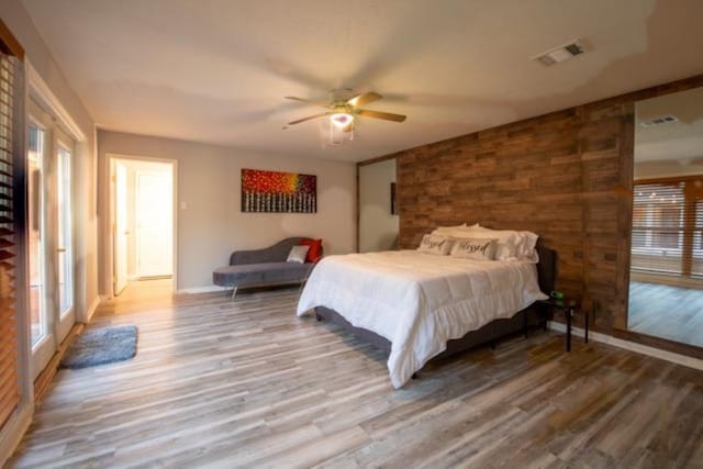 bedroom with a ceiling fan, visible vents, wood walls, and wood finished floors