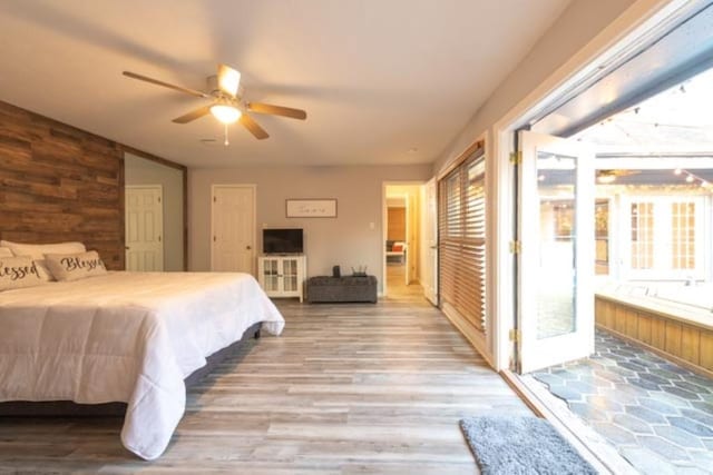 bedroom featuring multiple closets, a ceiling fan, wooden walls, ensuite bath, and wood finished floors