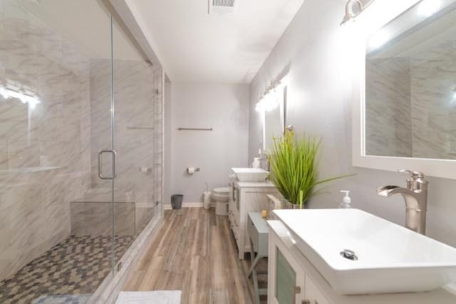 full bath with toilet, wood finished floors, visible vents, vanity, and a marble finish shower