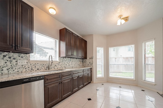 kitchen with light stone counters, stainless steel dishwasher, backsplash, and sink