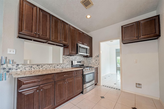 kitchen with light stone counters, light tile patterned flooring, decorative backsplash, dark brown cabinets, and appliances with stainless steel finishes