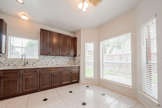 kitchen with backsplash, light stone countertops, sink, dark brown cabinets, and light tile patterned flooring