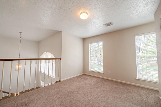 unfurnished room with a textured ceiling, a chandelier, and carpet flooring