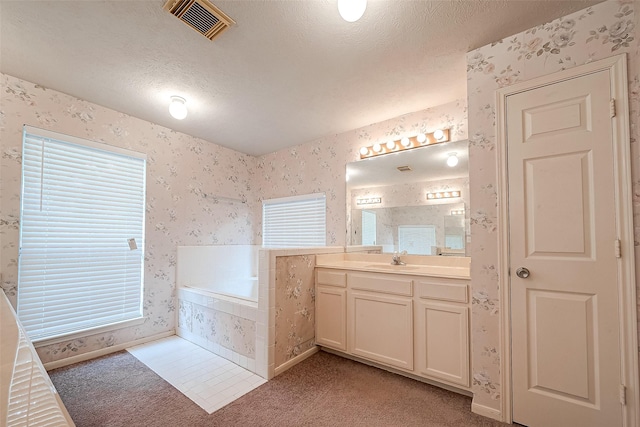 bathroom with a textured ceiling, tiled tub, and vanity