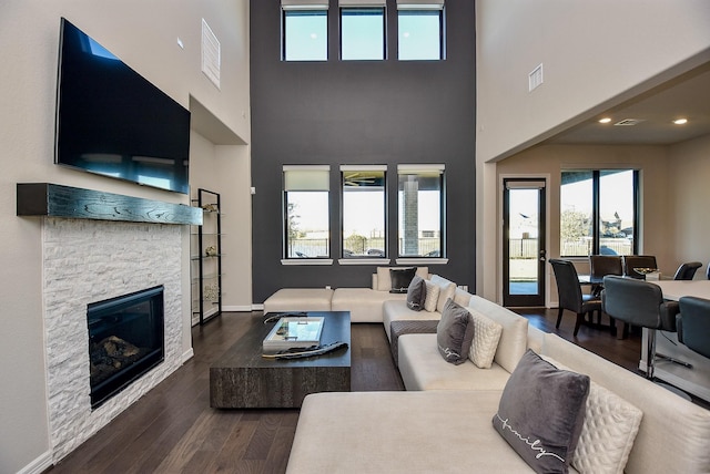 living room with a high ceiling, dark hardwood / wood-style flooring, and a stone fireplace