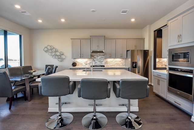 kitchen with dark wood-type flooring, a center island with sink, a breakfast bar, appliances with stainless steel finishes, and sink