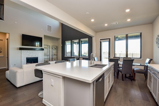 kitchen featuring dishwasher, a kitchen island with sink, a fireplace, sink, and white cabinetry