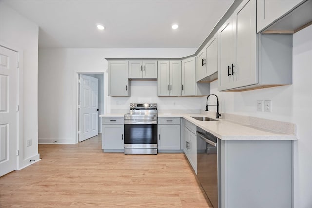 kitchen with appliances with stainless steel finishes, light hardwood / wood-style floors, gray cabinets, and sink