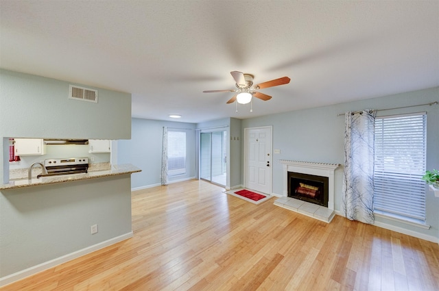 unfurnished living room with a tiled fireplace, ceiling fan, light hardwood / wood-style flooring, and plenty of natural light