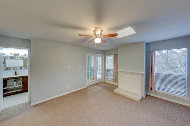 unfurnished living room featuring a textured ceiling, ceiling fan, carpet flooring, and a skylight