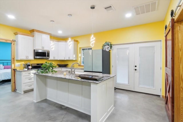 kitchen featuring a barn door, stainless steel appliances, hanging light fixtures, light stone counters, and white cabinets